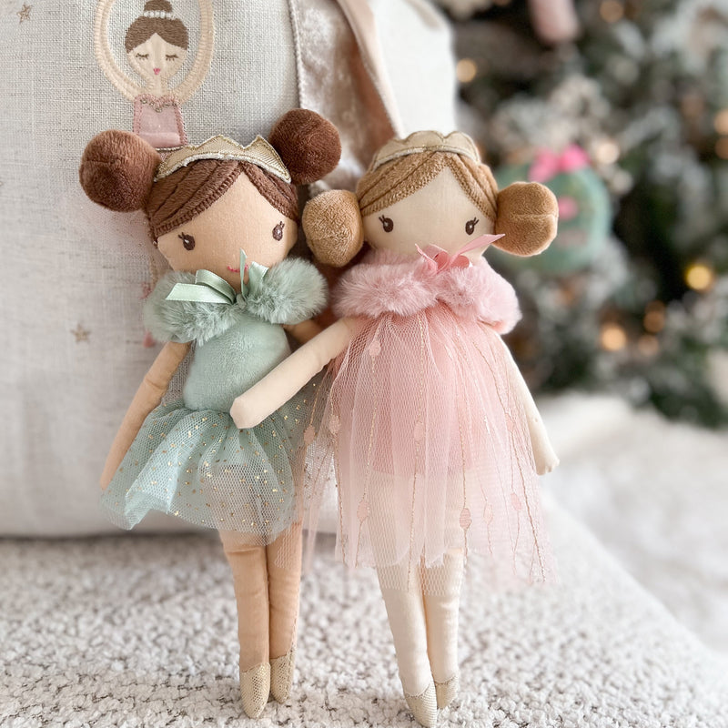 Two small dolls in pastel dresses standing in front of a decorated Christmas tree.
