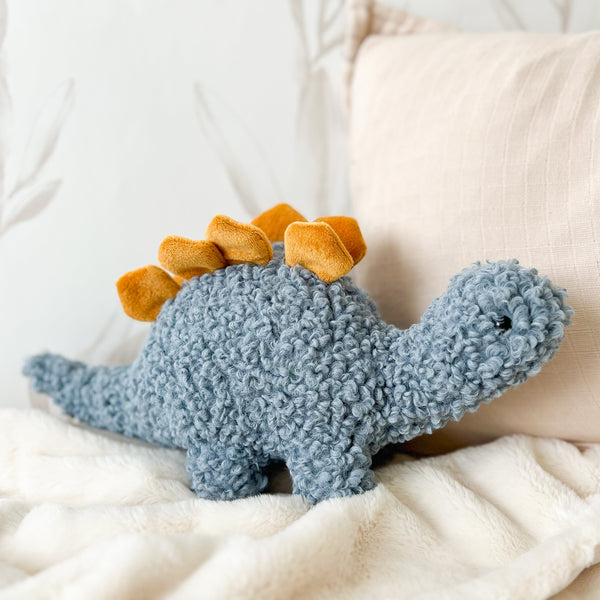 Blue plush dinosaur toy with orange spikes on a white surface