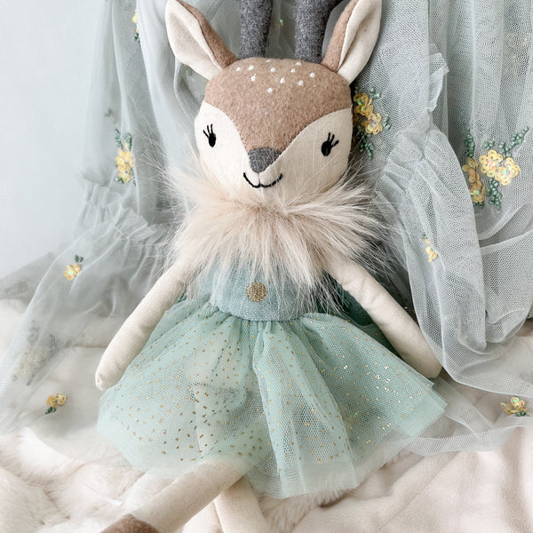 Stuffed deer toy with a green dress on a soft white background