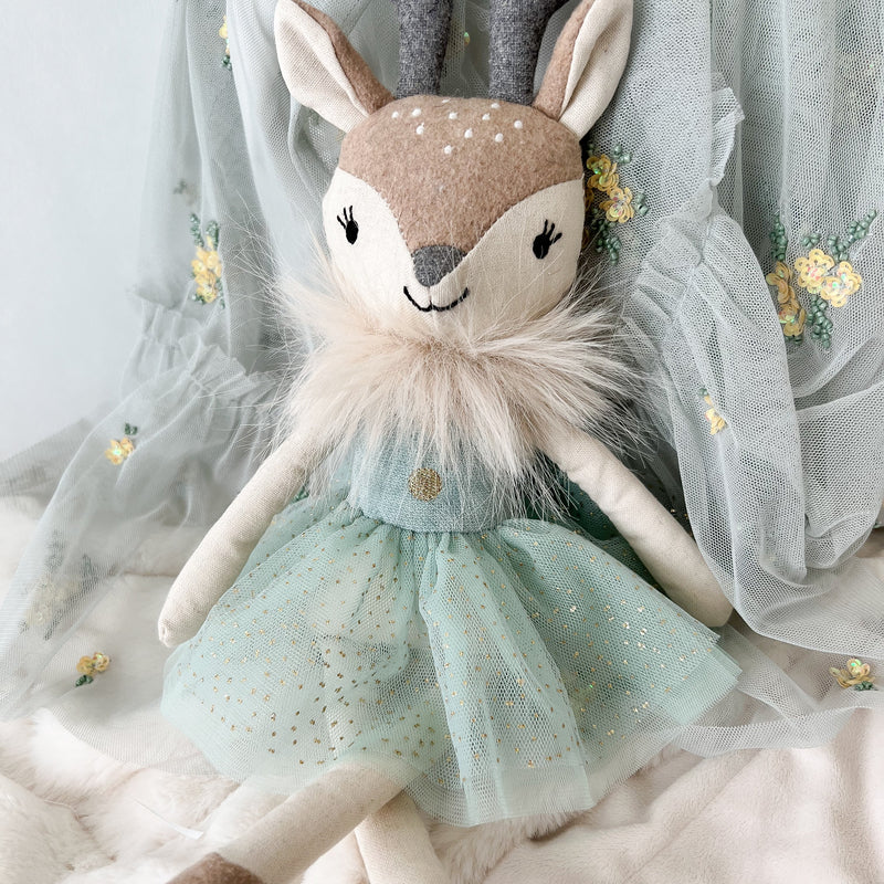 Stuffed deer toy with a green dress on a soft white background