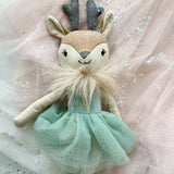 Stuffed deer toy with a green dress on a light pink fabric background