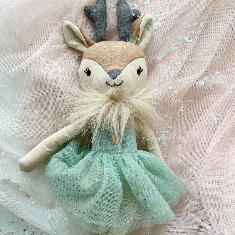 Stuffed deer toy with a green dress on a light pink fabric background