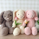 Four plush bunnies in gray, beige, pink, and green sitting together on a wooden surface.
