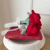 Red flower arrangement on a book titled 'LOVE', placed on a white round stand.